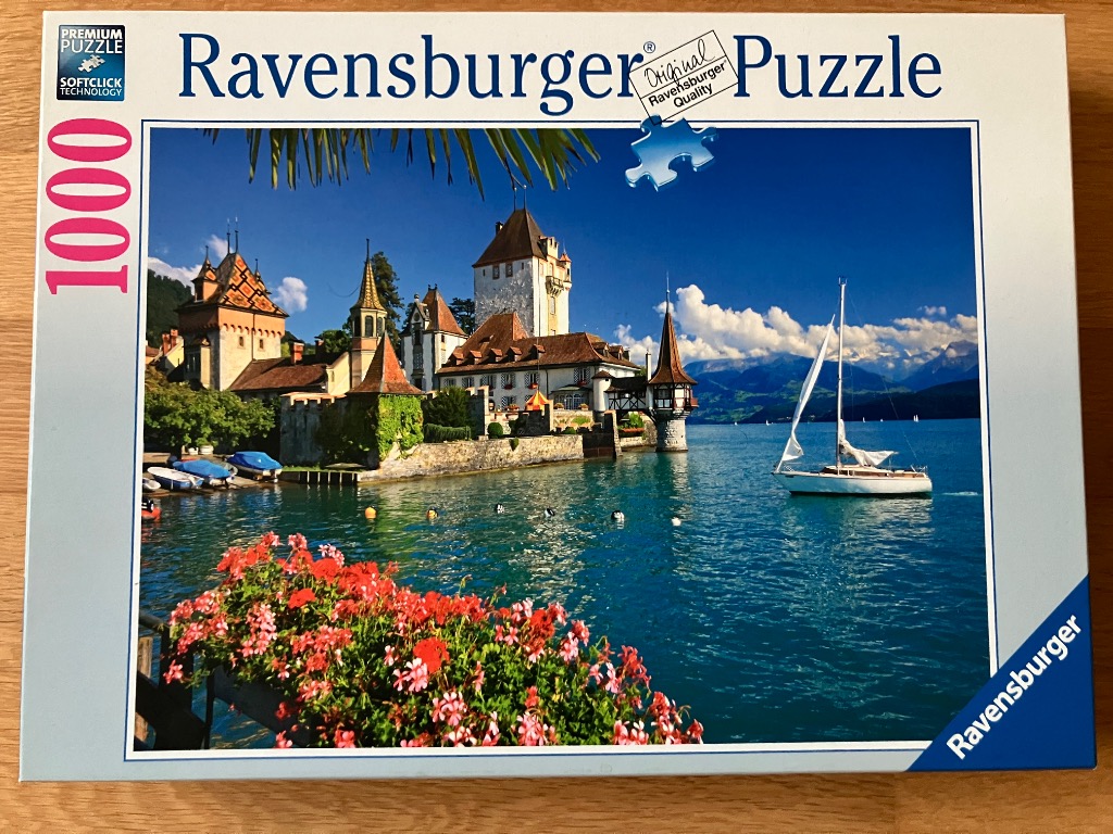 A sunny, scenic view of Oberhofen Castle on Lake Thun in Switzerland with a sailboat in the foreground.