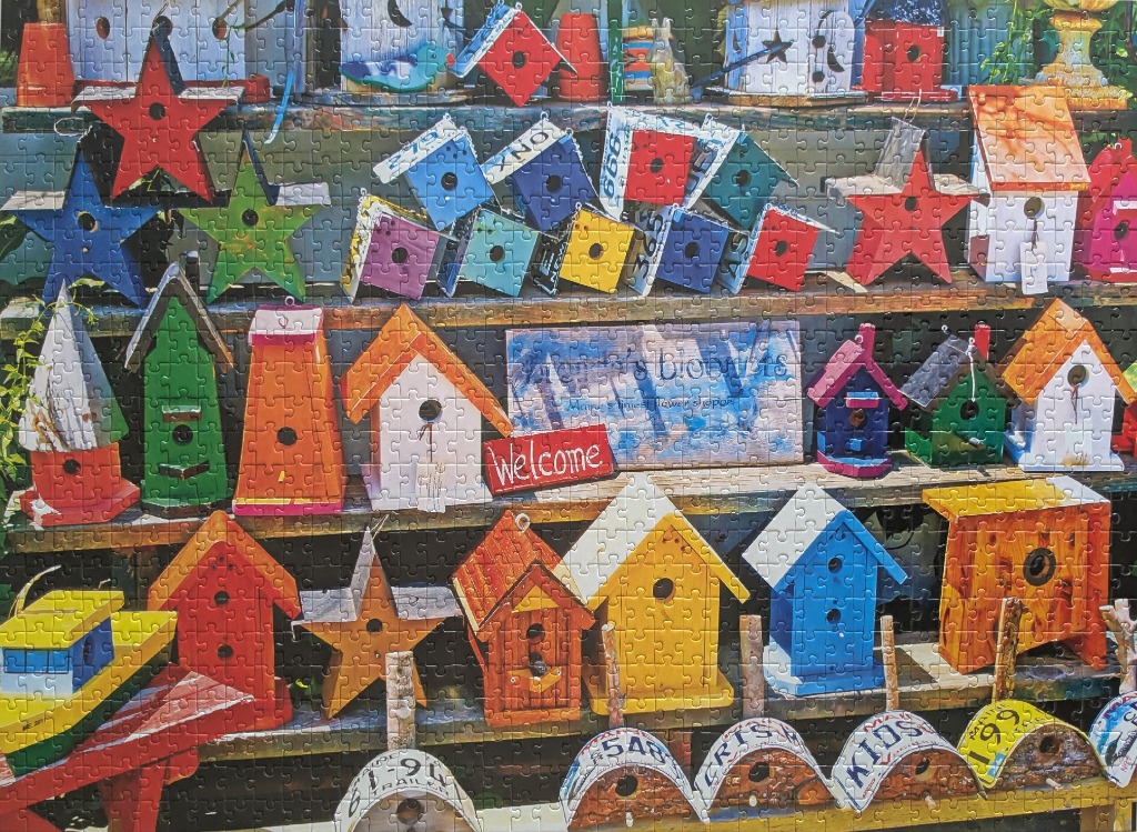 A vibrant display of numerous colorful birdhouses and star-shaped decorations arranged on tiered wooden shelves.