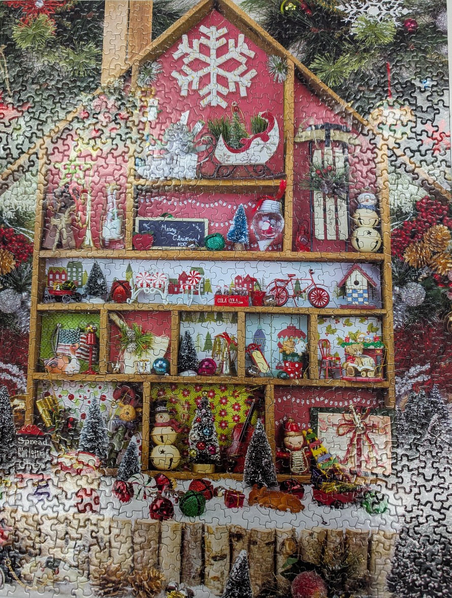 A whimsical Christmas-themed shelf unit shaped like a house, filled with miniature holiday decorations.