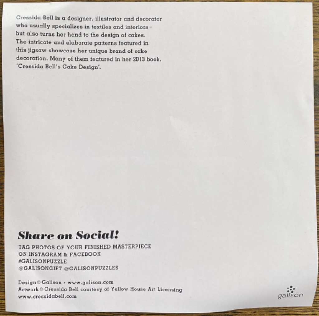 A white paper with printed text describing a designer and social media instructions, set against a wooden background.