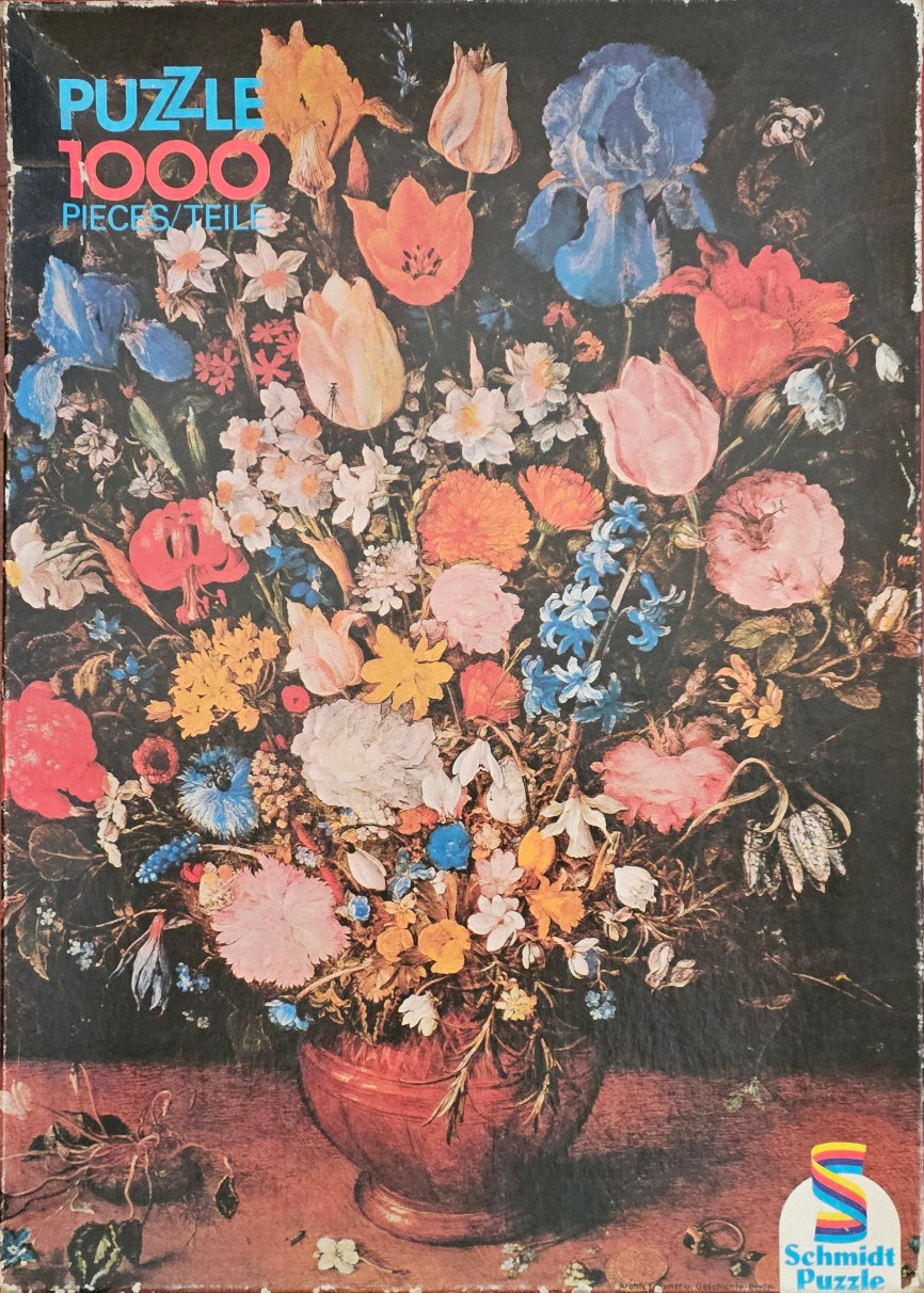 A lush, diverse bouquet of colorful spring flowers arranged in a round copper-toned vase against a dark background.