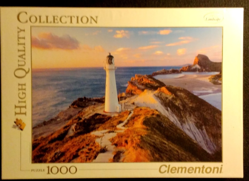 A scenic coastal landscape featuring a white lighthouse perched on a rugged cliffside at sunset.