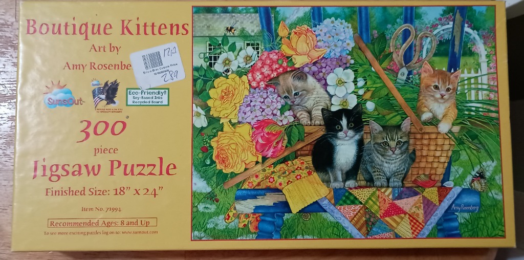 Four kittens nestled in a garden basket with flowers and a quilt on a blue wooden bench.
