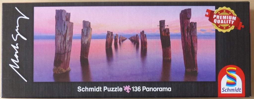 A panoramic landscape photograph of wooden jetty pylons rising from calm water at sunset.