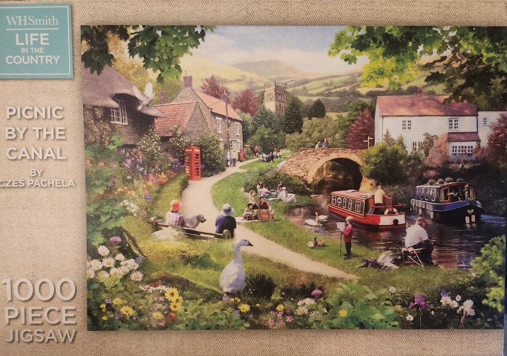 A peaceful English countryside scene by a canal with stone cottages, narrowboats, and people enjoying a picnic.
