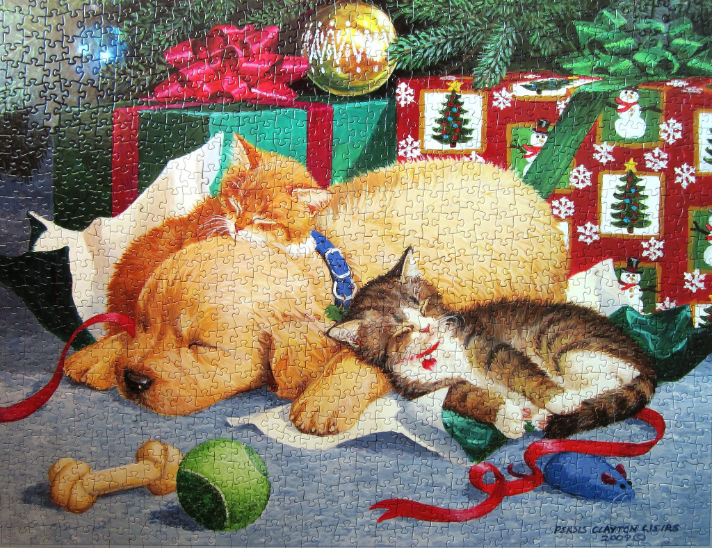A golden retriever puppy and two kittens sleeping together under a Christmas tree surrounded by gifts.