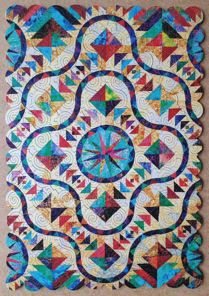 A quilt-inspired pattern featuring colorful geometric shapes, central starbursts, and flowing dark blue curved lines.