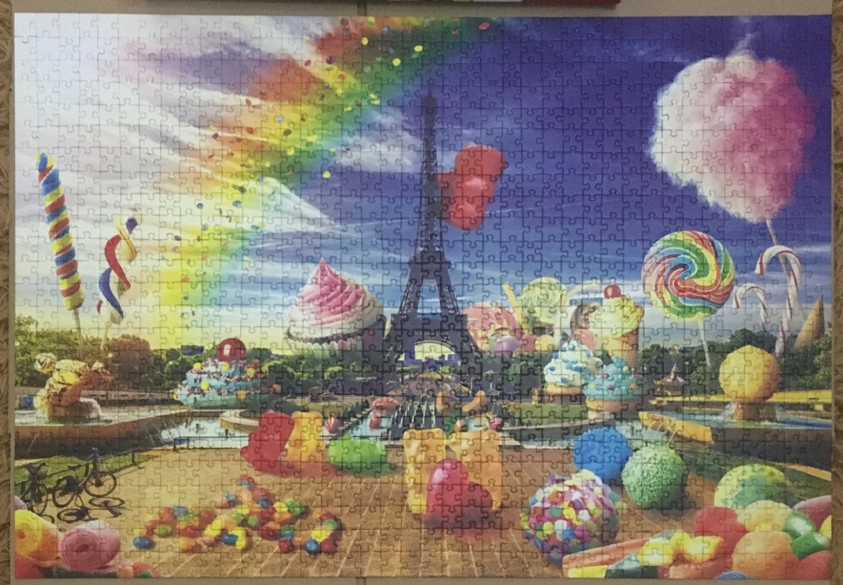 Surreal illustration of the Eiffel Tower surrounded by giant candy and sweets under a rainbow sky.