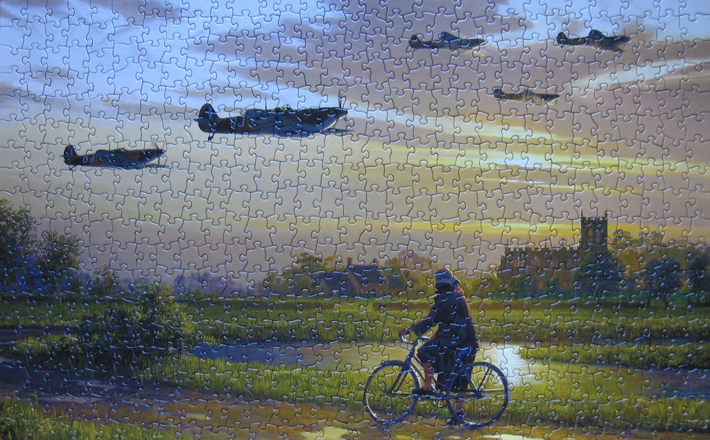 A person on a bicycle watches a squadron of Spitfire fighter planes flying over a quiet English village at sunset.