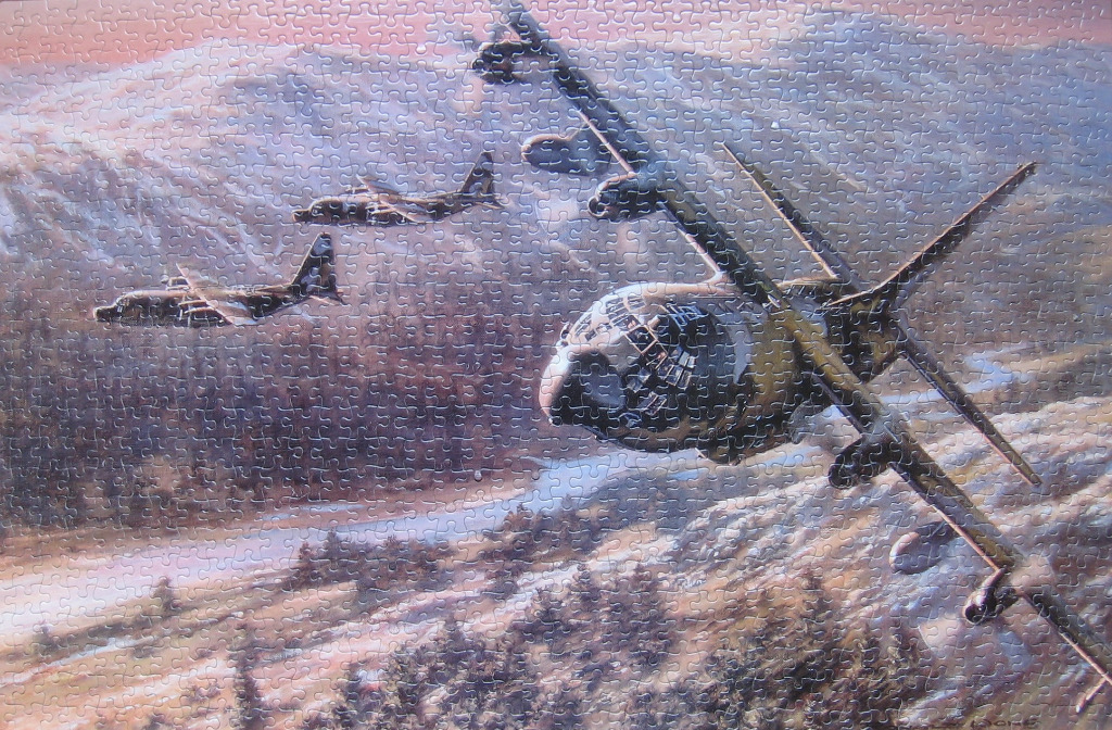 Three military transport aircraft flying in formation over a mountainous landscape at sunset.