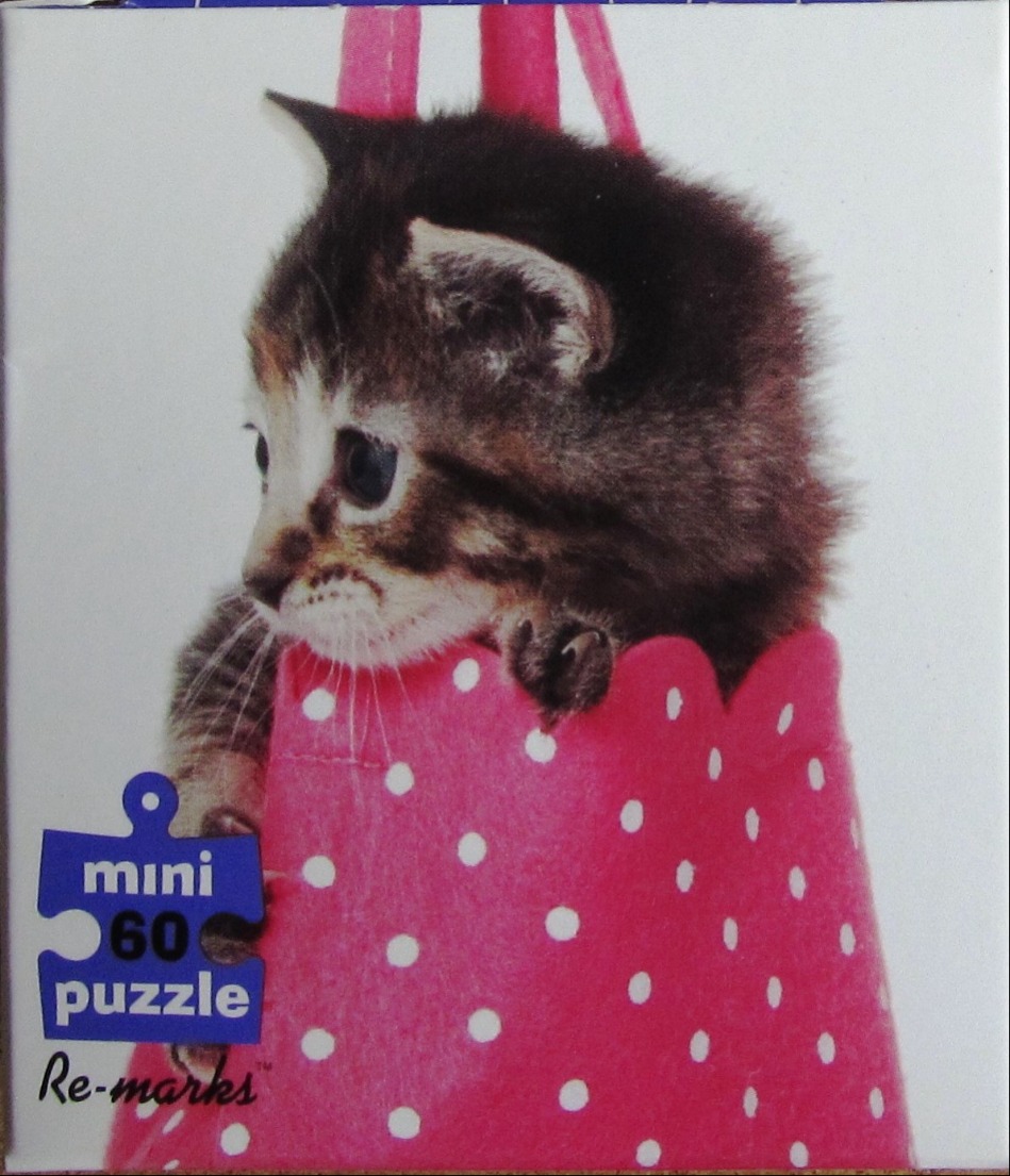 A small, brown, tabby kitten sitting inside a bright pink polka-dot felt bag.
