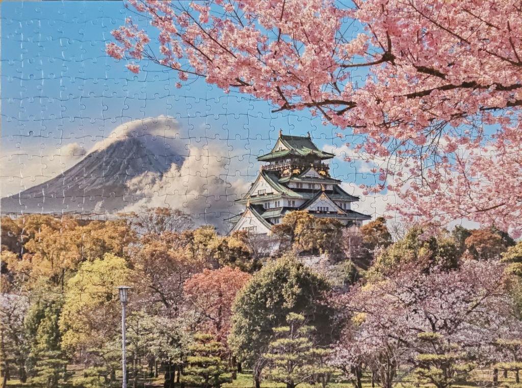 A Japanese castle surrounded by cherry blossoms with a snow-capped mountain in the background.