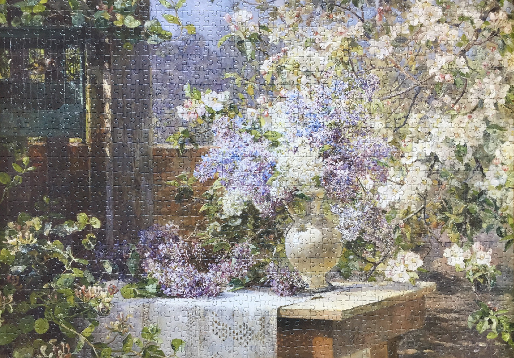 A floral still life featuring a white vase of lilacs on a table in a blooming spring garden.