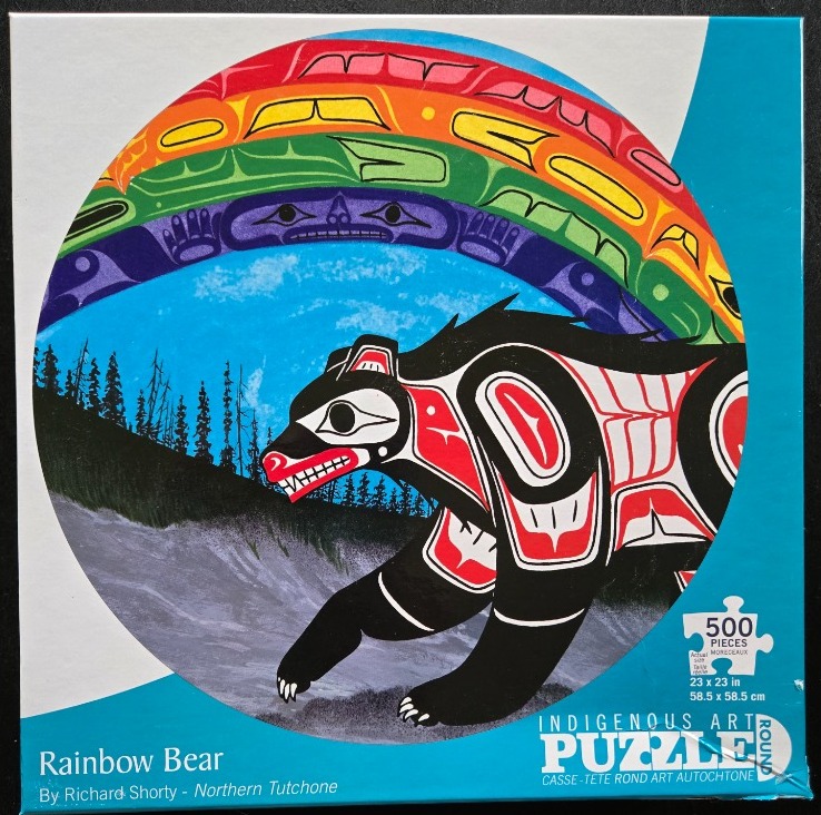 A stylized bear in Northwest Coast Indigenous art style beneath a vibrant rainbow arching over a dark, silhouetted forest.