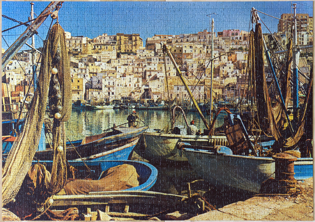 A sunny harbor scene in Italy with fishing boats in the foreground and stacked hillside buildings in the background.