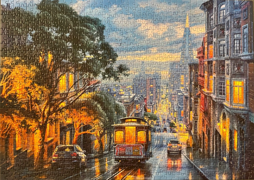A San Francisco cable car traveling down a steep, tree-lined street at sunset.