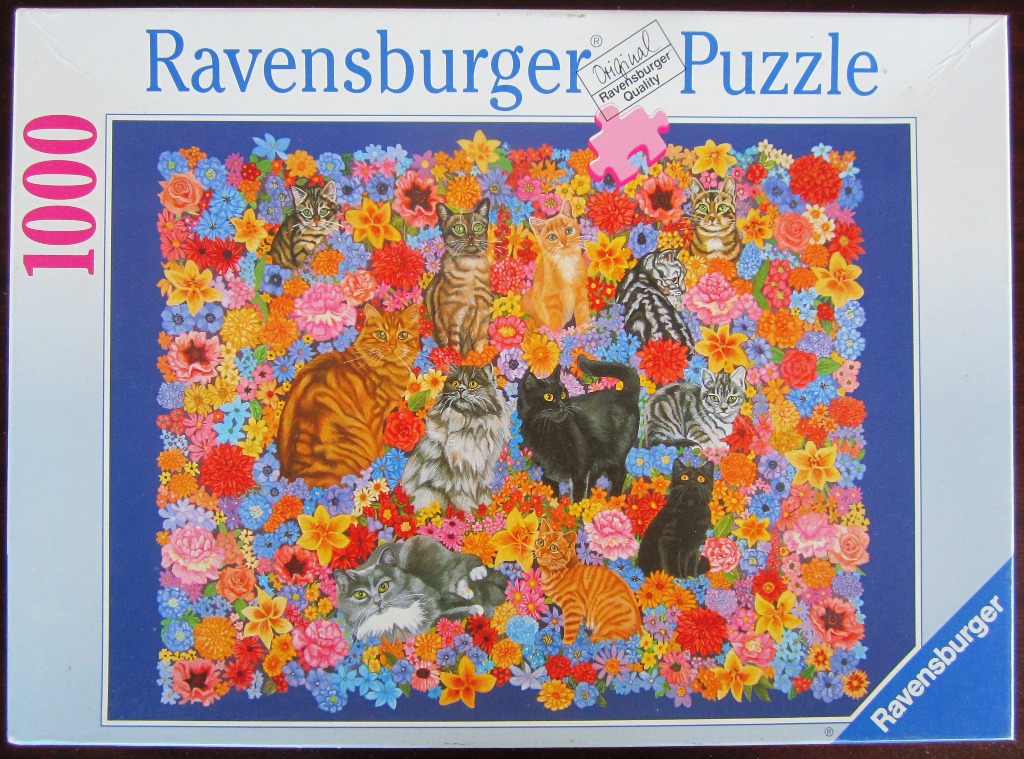 A collection of eleven domestic cats of various breeds and colors sitting amongst a dense, colorful field of flowers.