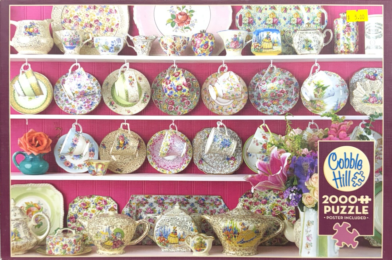 A collection of vintage floral teacups, saucers, and teapots displayed on white shelves against a bright pink background.