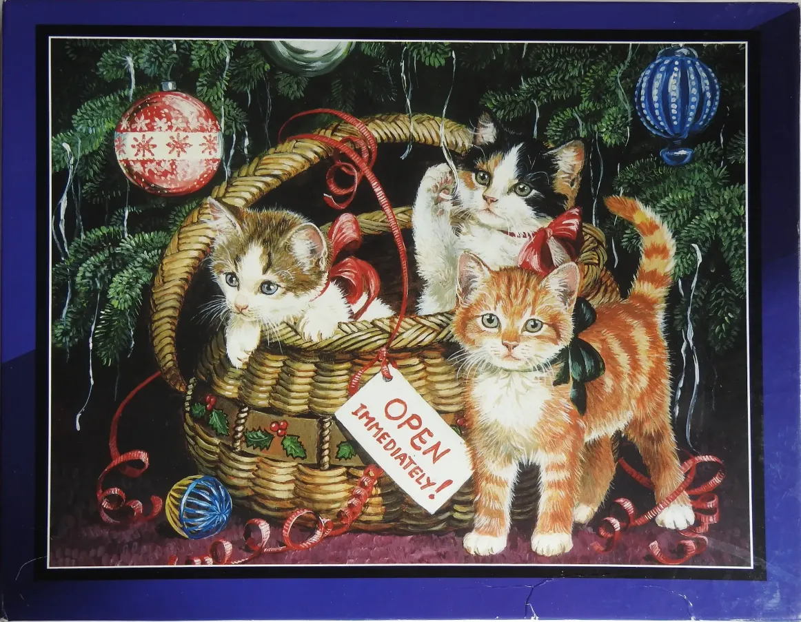 Three kittens playing in a wicker basket beneath a decorated Christmas tree.