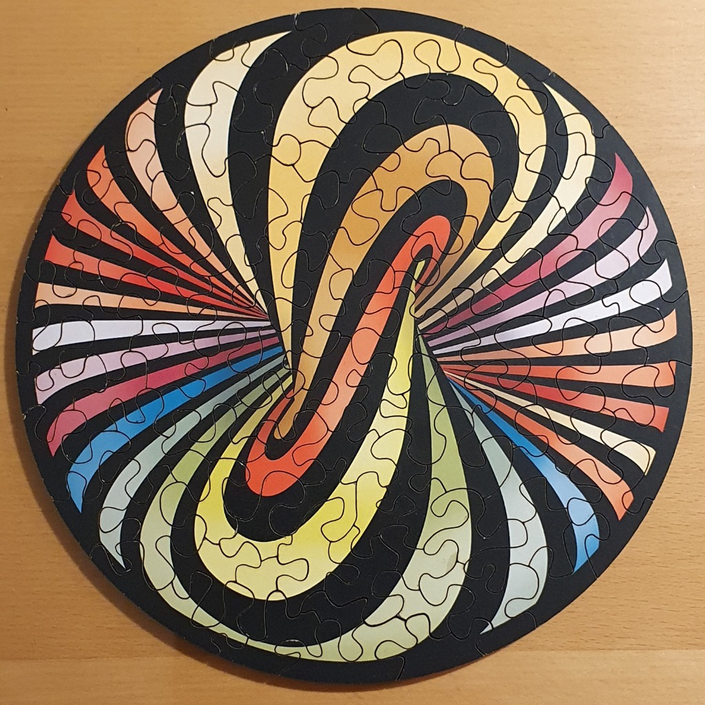 A circular abstract design featuring swirling, multi-coloured radial bands against a solid black background.