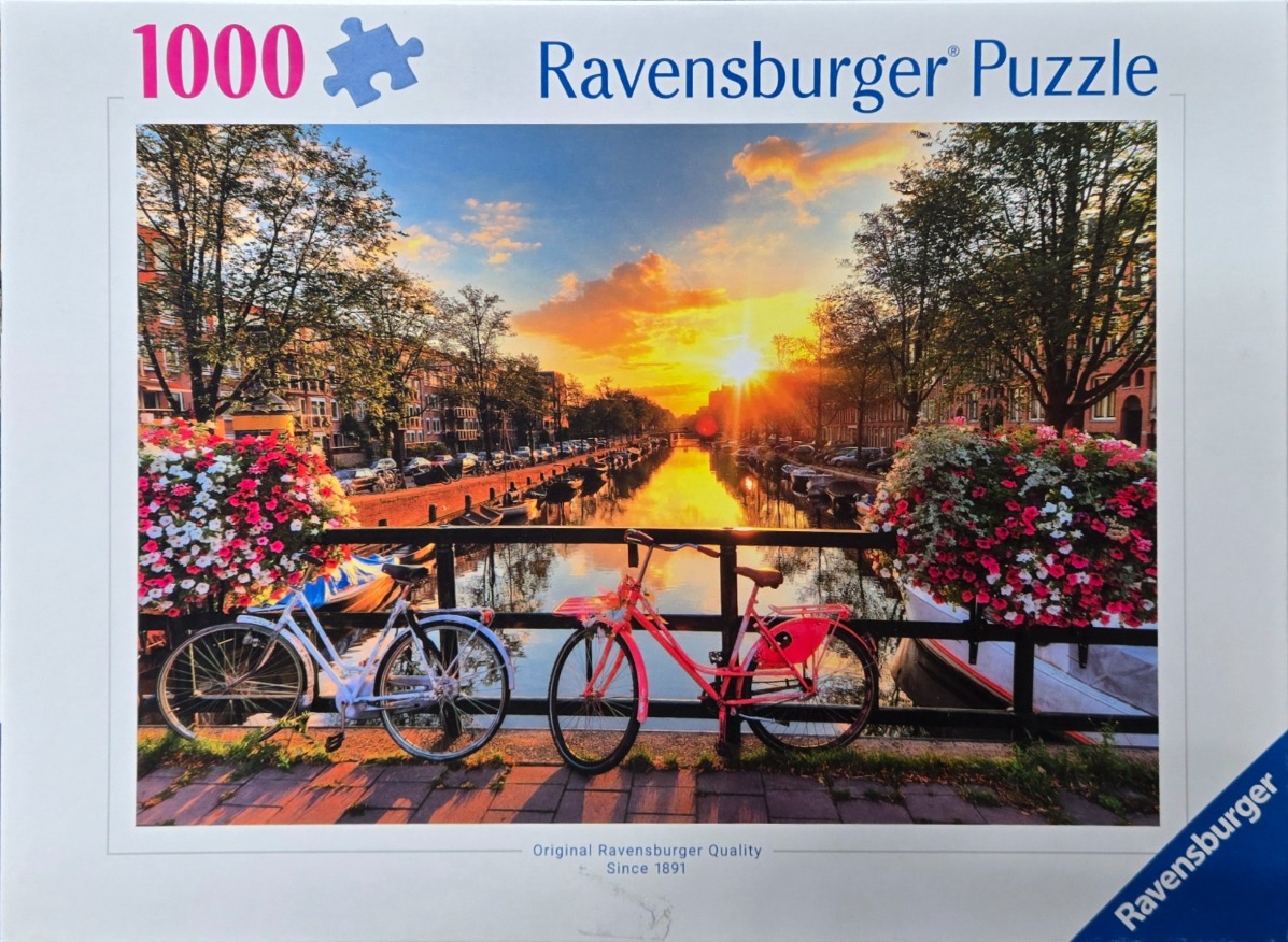 Two bicycles parked on a canal bridge in Amsterdam at sunset with overflowing flower baskets.