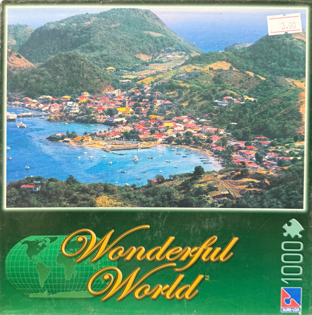 Aerial view of a colorful coastal town nestled between lush green mountains and a deep blue bay.