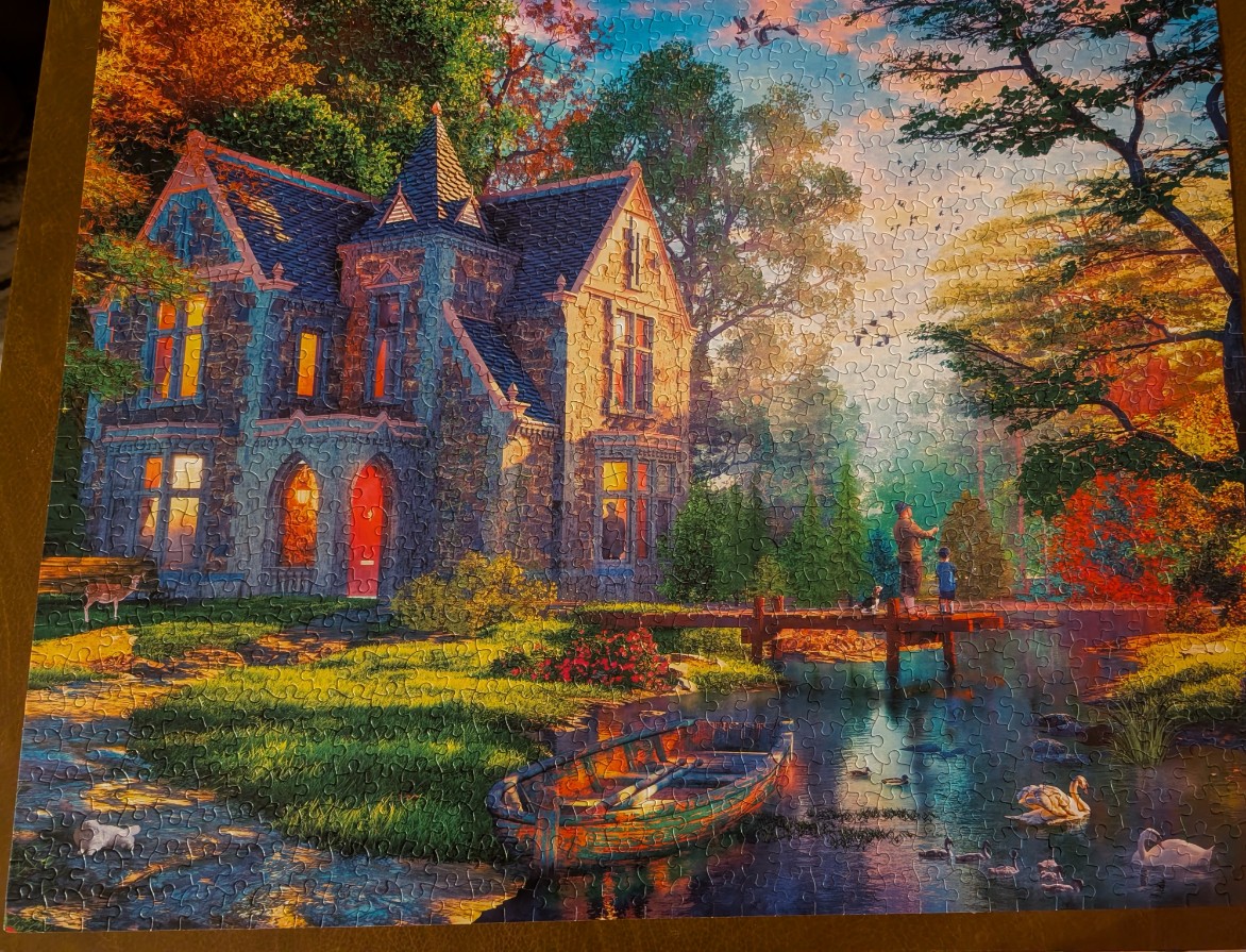 A stone cottage beside a stream at sunset with a person fishing and swans in the water.