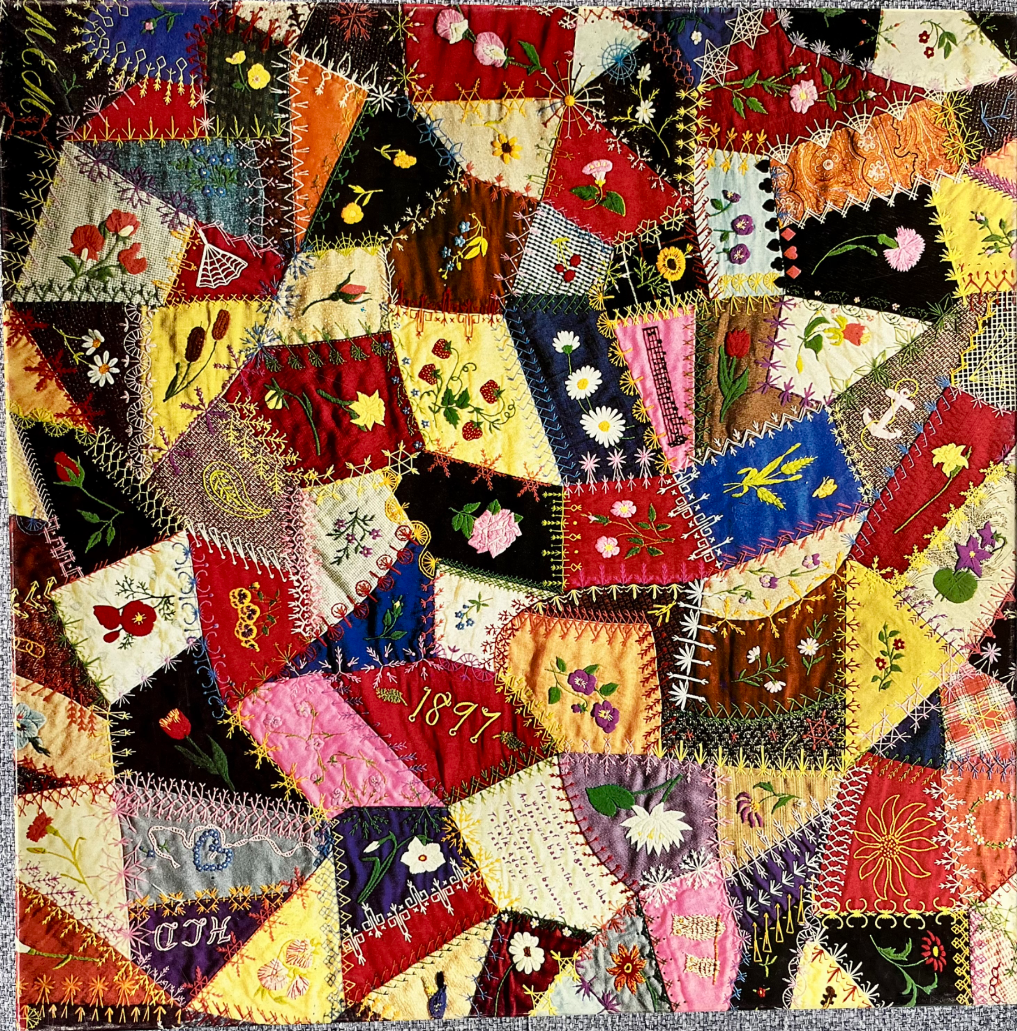 A close-up of a Victorian-era crazy quilt with vibrant, multi-coloured fabric patches and intricate embroidery.