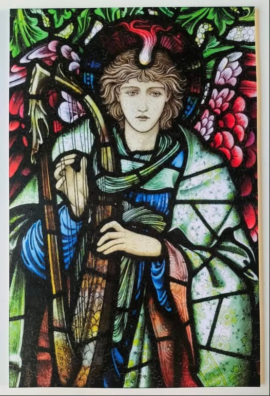 Stained glass illustration of an angel with wavy hair playing a harp.