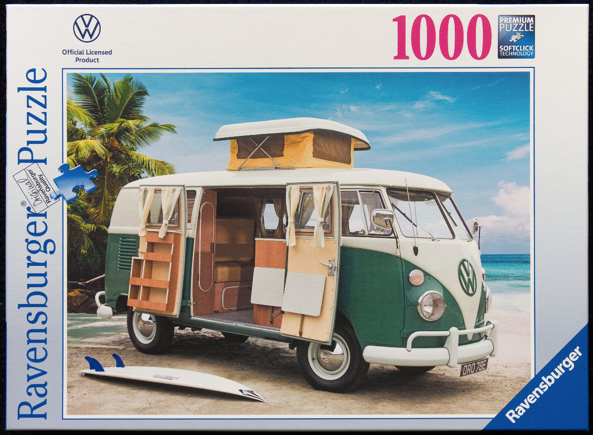 A vintage green and white VW camper van parked on a tropical sandy beach with a surfboard in the foreground.