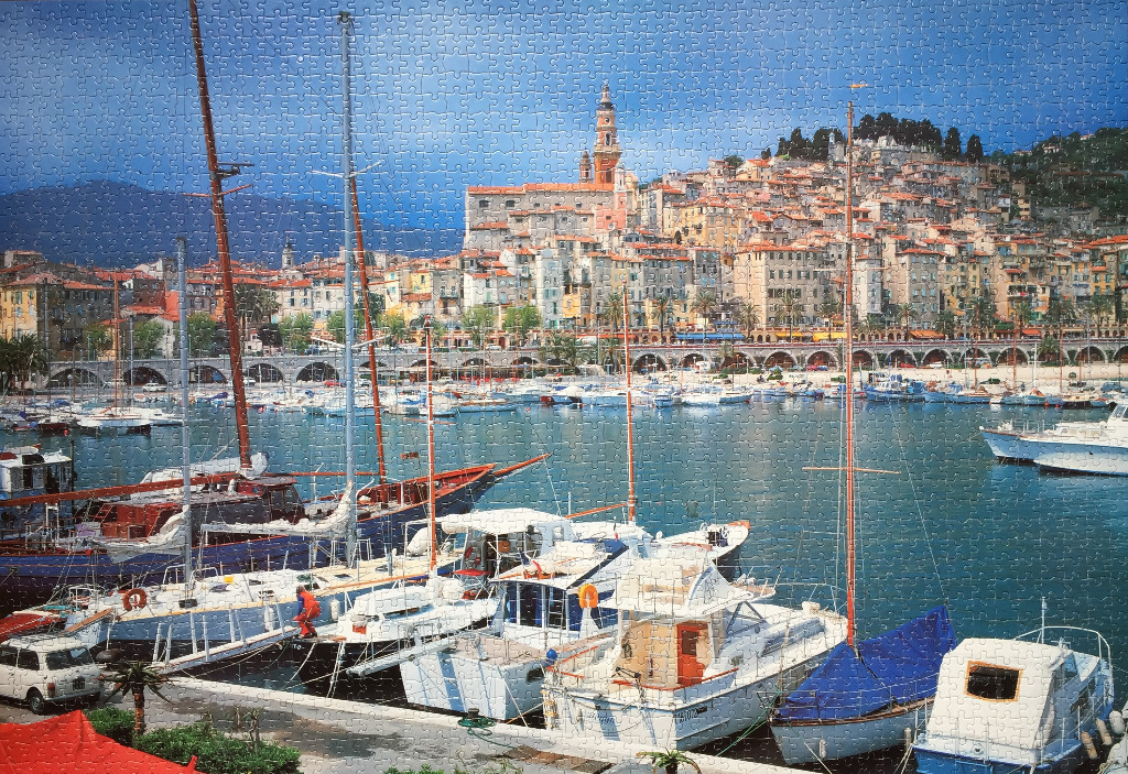 A panoramic view of the Menton harbor in France with boats in the foreground and a Mediterranean hillside town behind.