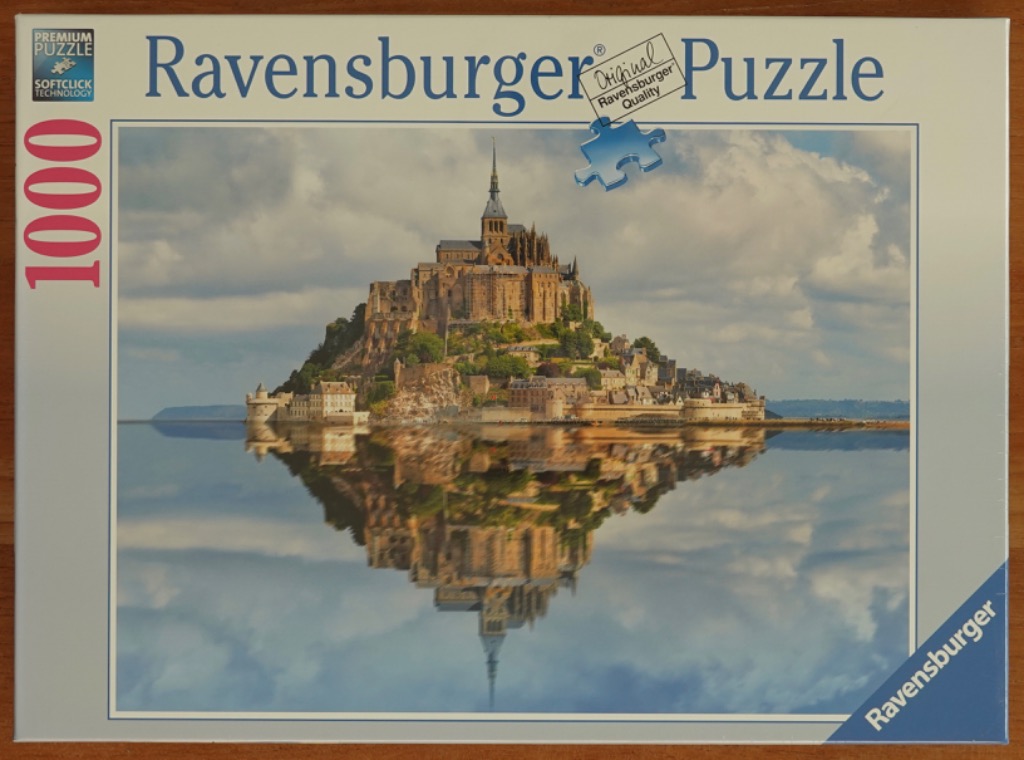 Mont Saint-Michel abbey on a tidal island reflected in calm water under a cloudy sky.