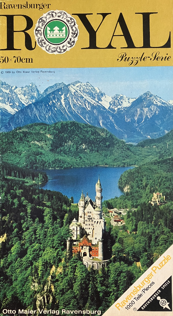 A photograph of Neuschwanstein Castle nestled in a lush green forest with a mountain lake and snowy peaks in the background.