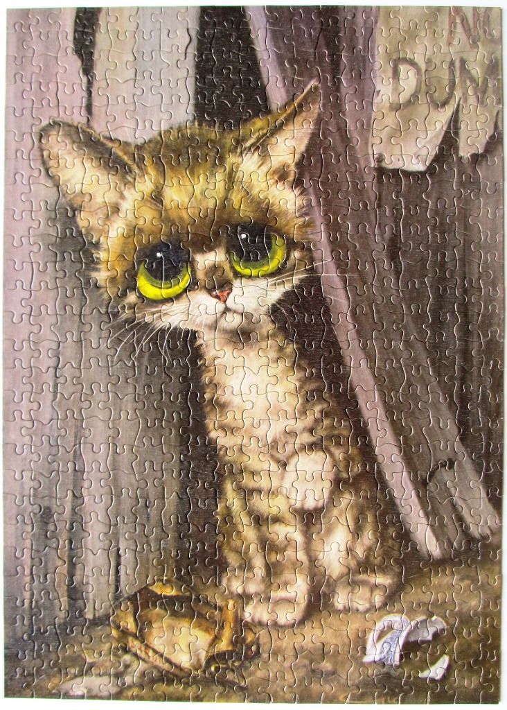 A sad-looking tabby kitten with oversized green eyes sits in front of a wooden fence.