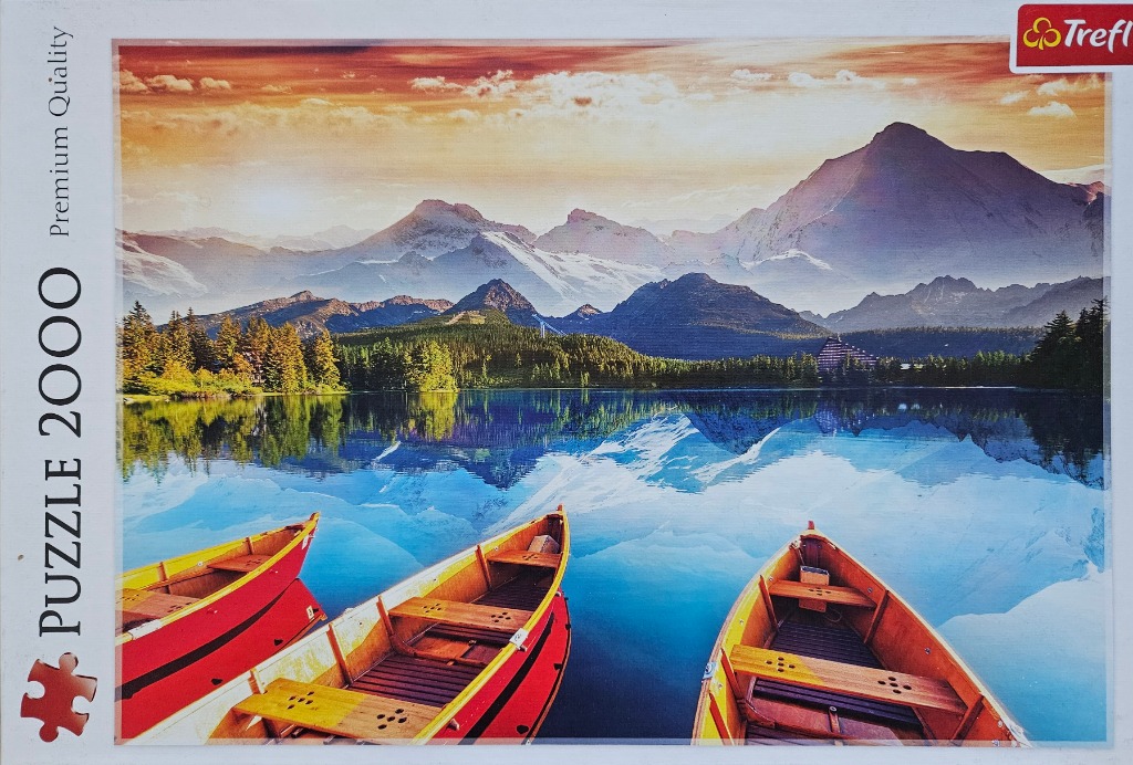Three wooden rowboats floating on a calm lake reflecting snow-capped mountains at sunrise.