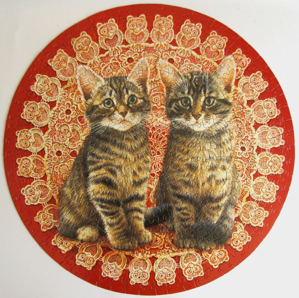 Two tabby kittens sitting on an ornate red and white owl-patterned lace doily.