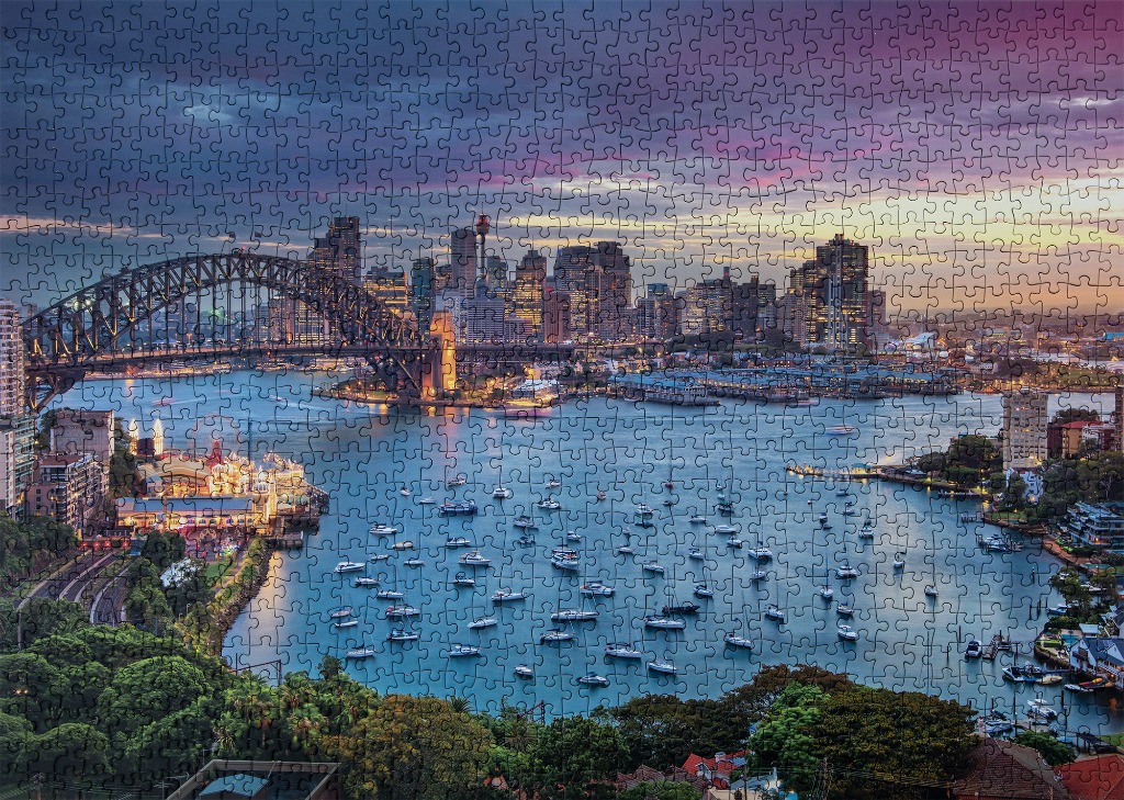 Sydney Harbor at sunset featuring the Harbour Bridge and a dense fleet of anchored boats.