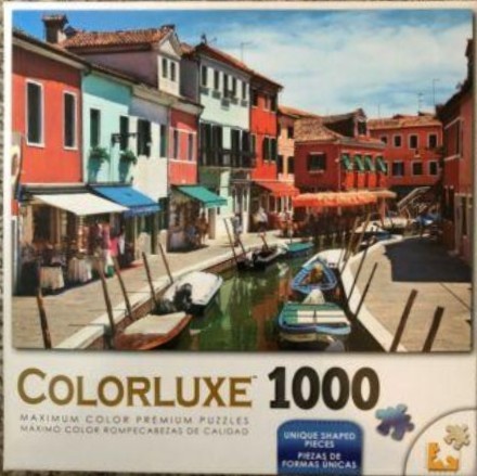 A sunny canal scene in Burano, Italy, with brightly colored buildings, small boats, and stone walkways.