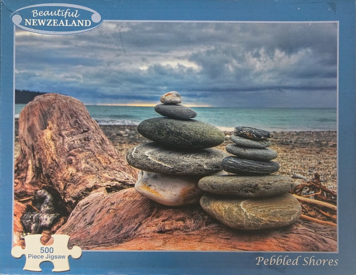 Two stone cairns stacked on a piece of weathered driftwood on a beach under a cloudy sky.