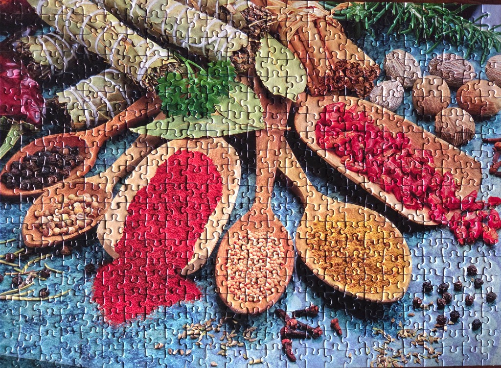Close-up overhead view of wooden spoons filled with colourful spices on a textured blue surface.