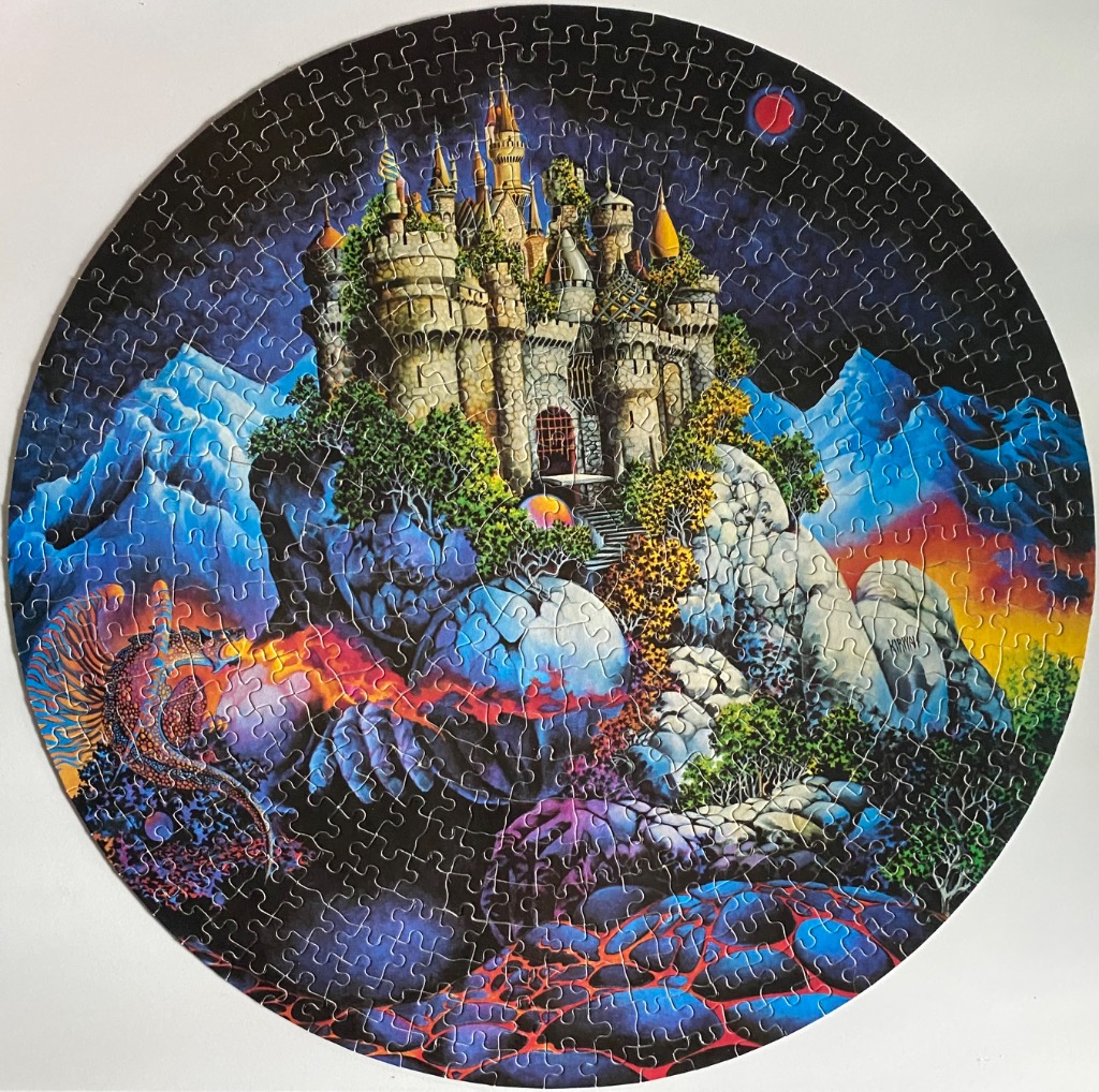 A circular fantasy illustration of a castle perched on a rocky crag with glowing lava and a mythical reptile.