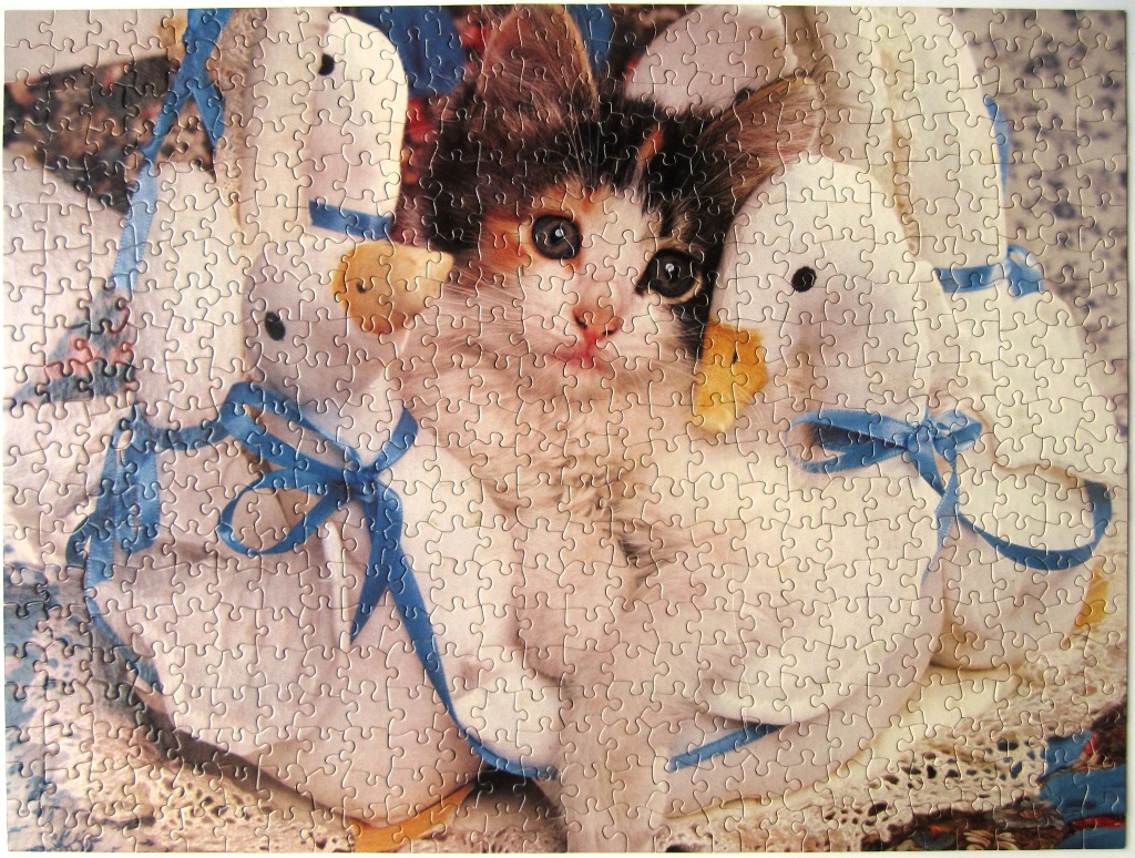 A calico kitten nestled between two plush white geese with blue ribbons