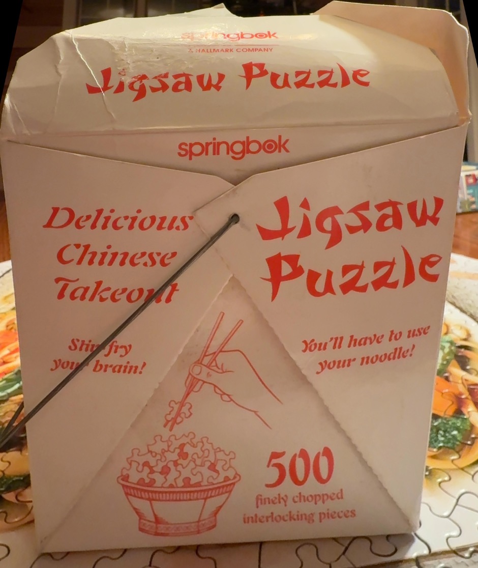 A square white carton with red Chinese-style text and an illustration of a hand lifting puzzle pieces with chopsticks.