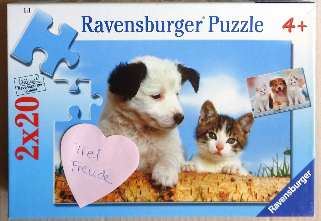 A puppy and a kitten sitting together behind a birch log, with a small heart-shaped note in the foreground.