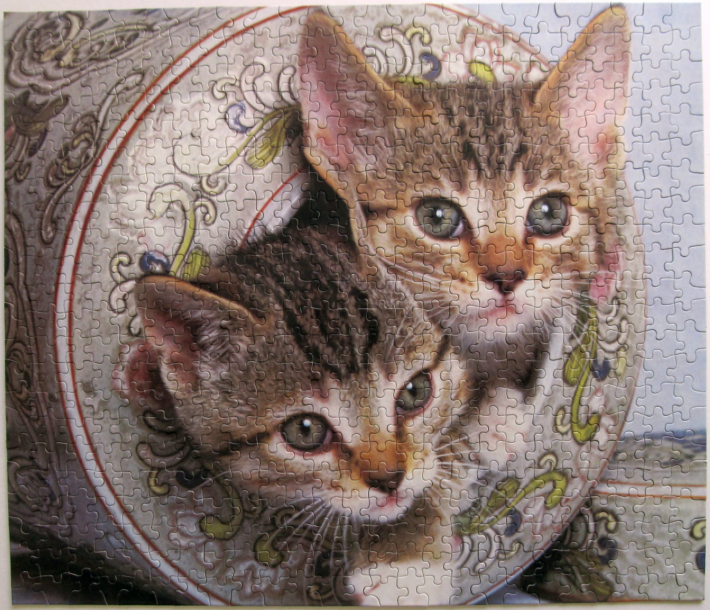 Two tabby kittens peeking out from inside an ornate, decorated porcelain bowl.
