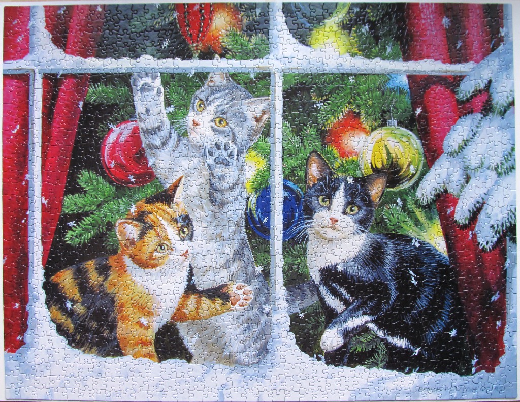 Three kittens sitting in a window frame looking at a Christmas tree with red curtains and snow outside.