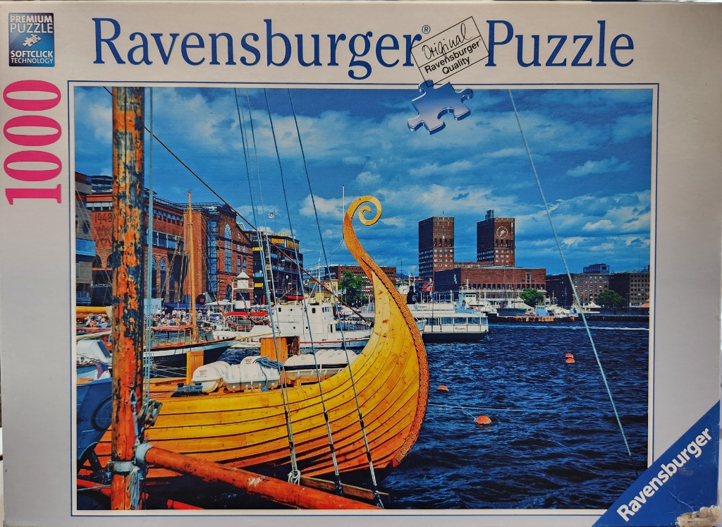 A Viking-style wooden ship docked in a harbor with a brick city skyline in the background.