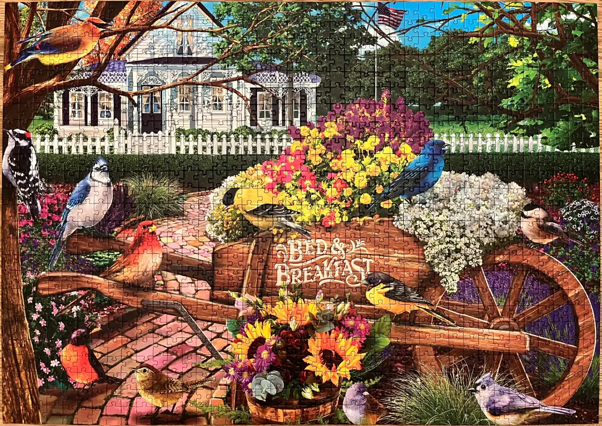 An idyllic garden scene featuring a rustic wooden wheelbarrow filled with flowers surrounded by various songbirds.