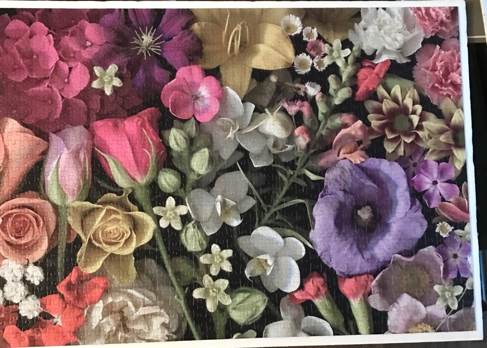 A lush, close-up arrangement of diverse flowers in shades of pink, purple, yellow, and white against a dark background.