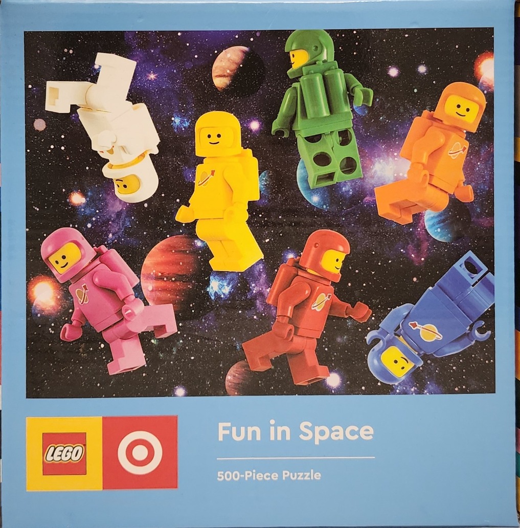 Six colorful plastic minifigure astronauts floating in deep space against a backdrop of stars and planets.